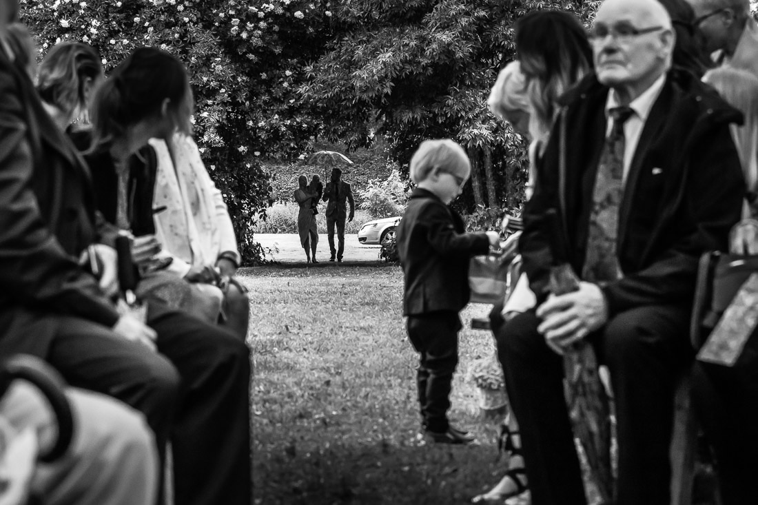 Barn vid ingången Litet barn vid ceremonins ingång medan brudparet anländer i svartvitt – bröllopsfotograf Skåne