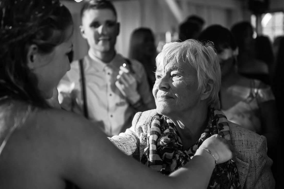 Kram med mormor Bruden i en rörd kram med en äldre kvinna under minglet i svartvitt – bröllopsfotograf Skåne