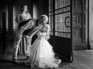 G&auml;st kysser en liten brudn&auml;bb i rosa kl&auml;nning vid kyrkporten &ndash; br&ouml;llopsfotograf Lund