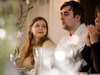 Brudparet kysser varandra vid f&ouml;nstret under middagen &ndash; br&ouml;llopsfotograf Lund