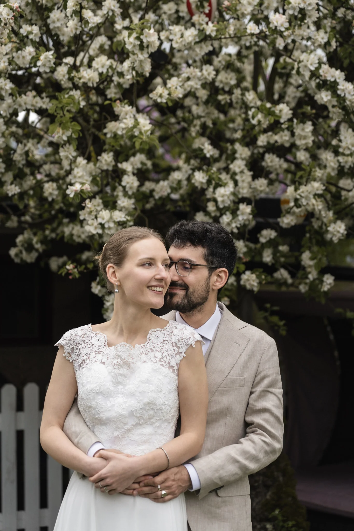 Brudparet under blommorna Brudpar omfamnas framför blommande äppelträd i trädgården i Malmö – bröllopsfotograf Malmö