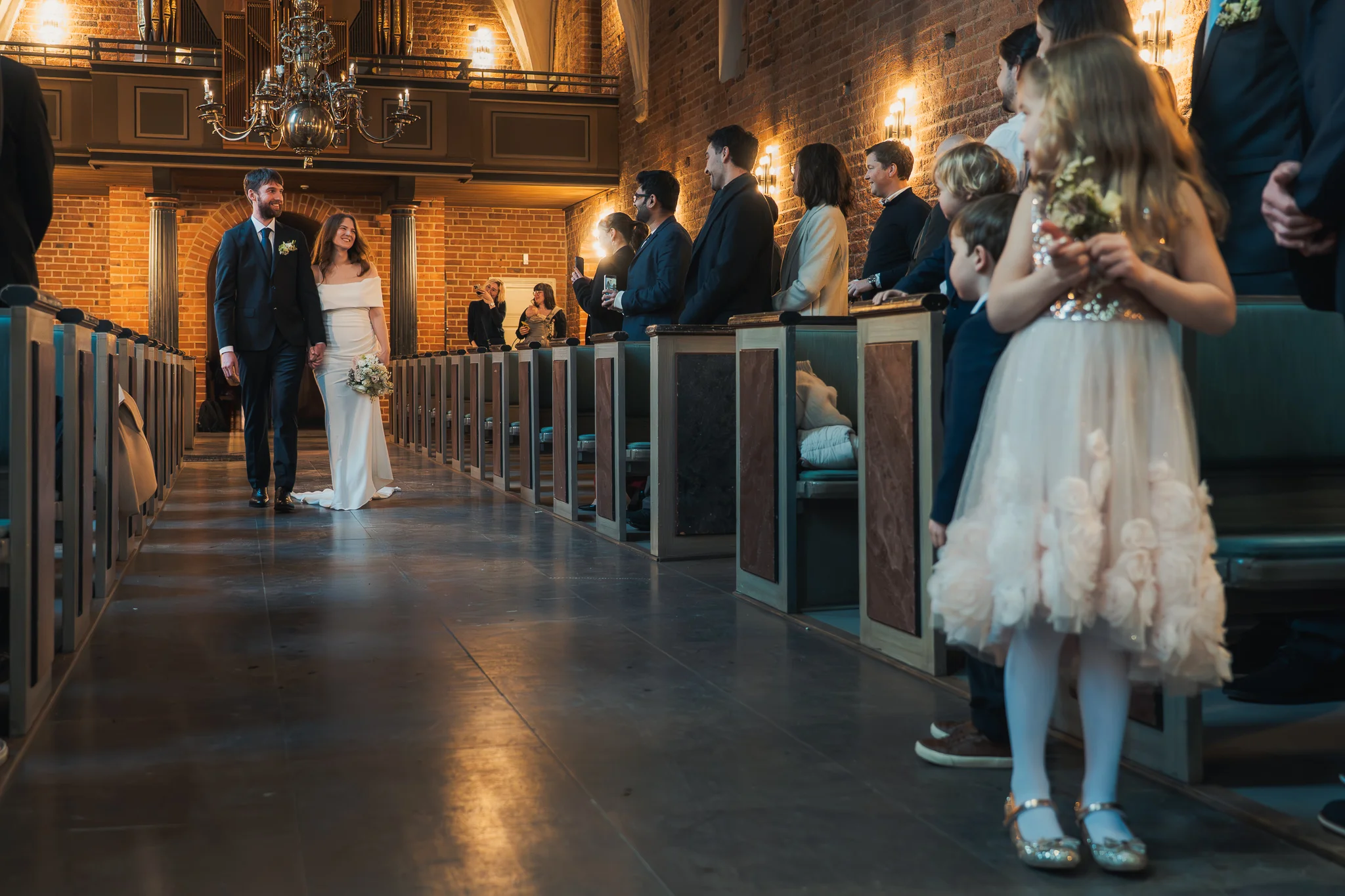 Bruden och brudgummen går in Bruden och brudgummen går in i Klosterkyrkan medan gästerna ser på – bröllopsfotograf Lund