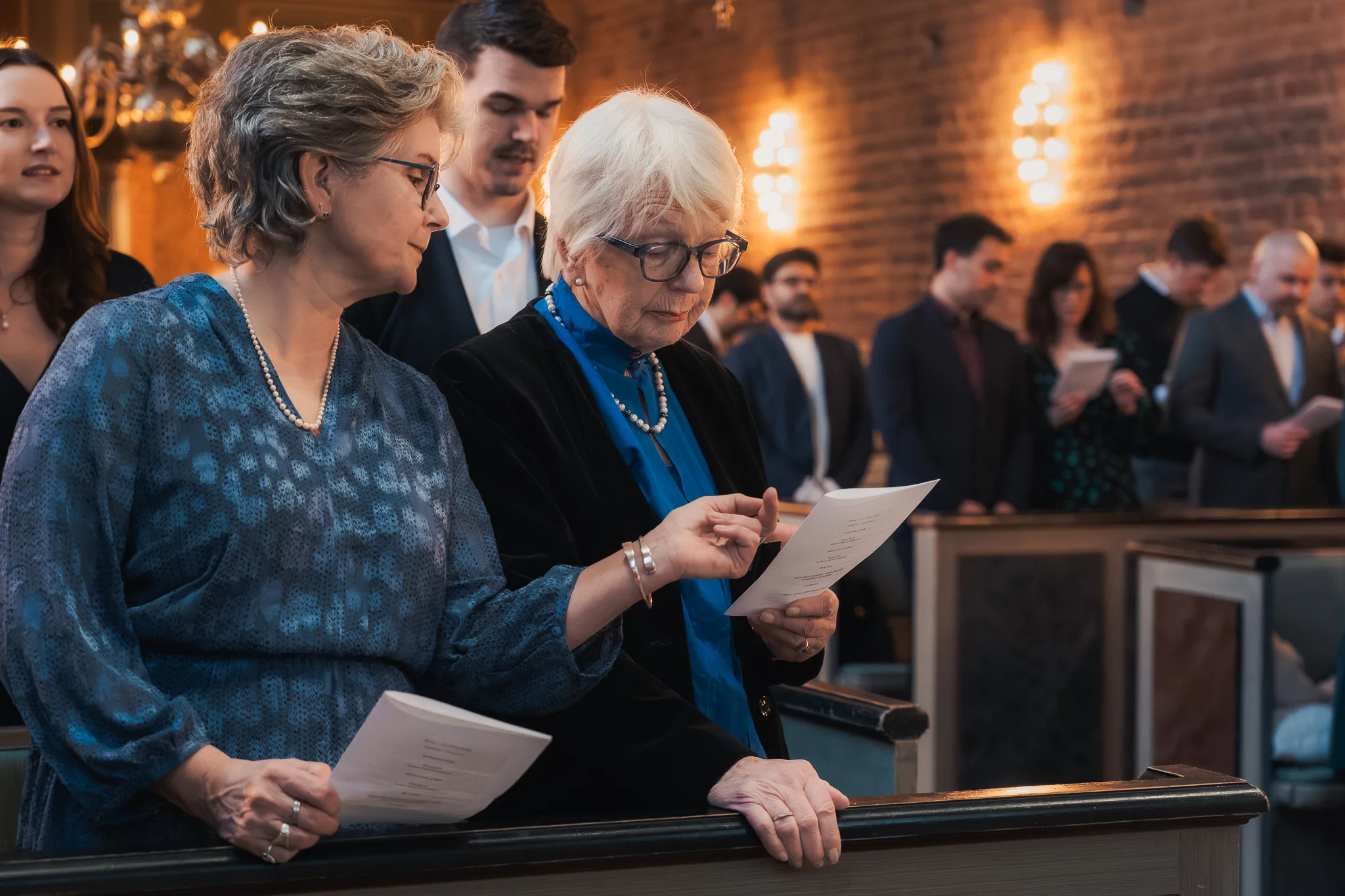 Familjen i bänkarna Gäster följer ceremonin ur programbladet i Klosterkyrkan i Lund – bröllopsfotograf Lund