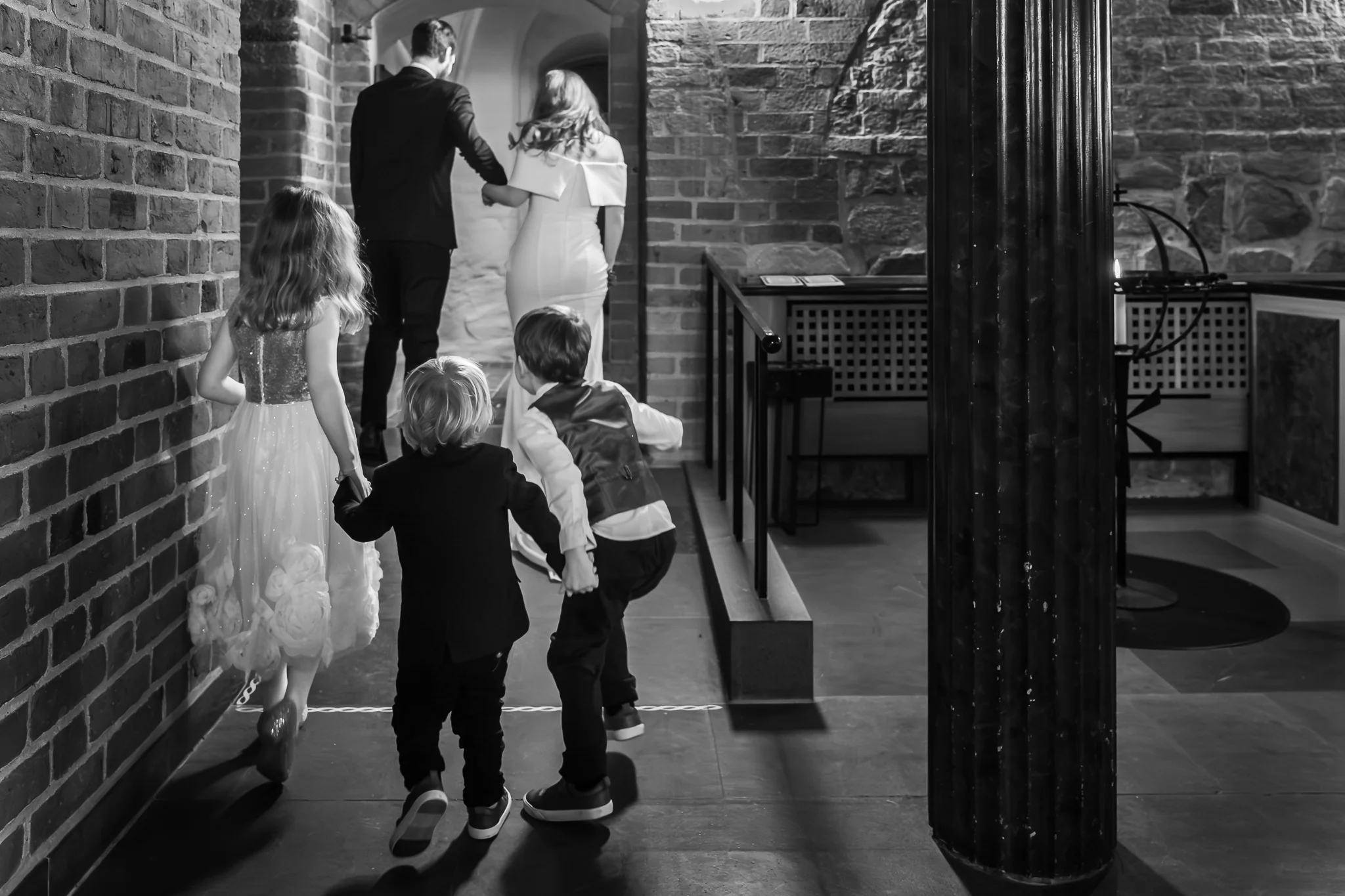 Barnen följer efter Barn följer efter paret ut genom Klosterkyrkans tegelgång i Lund – bröllopsfotograf Lund