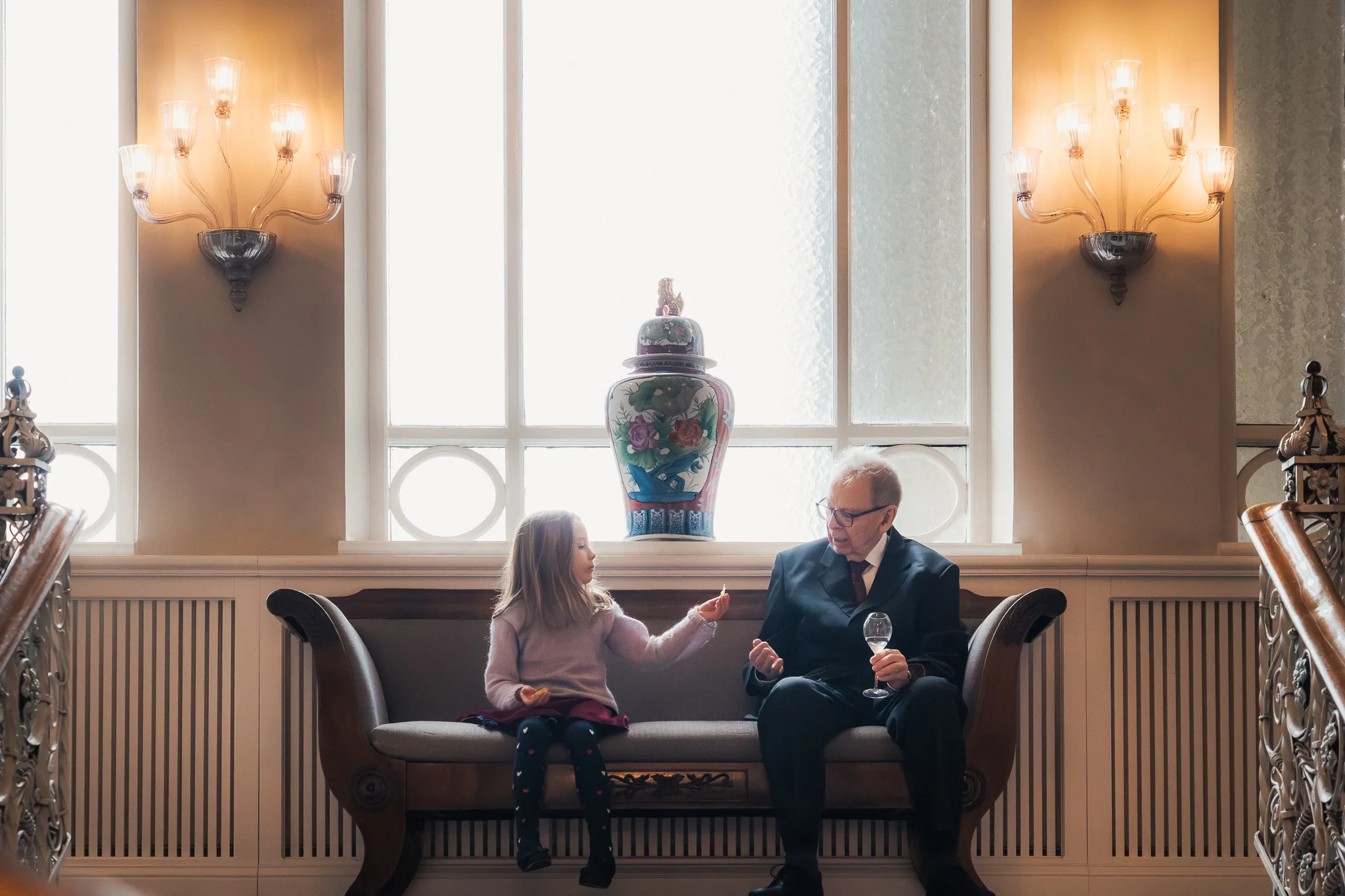 Vid fönstret på Grand Hotel Flicka och äldre gäst på bänk vid fönstret på Grand Hotel i Lund – bröllopsfotograf Lund