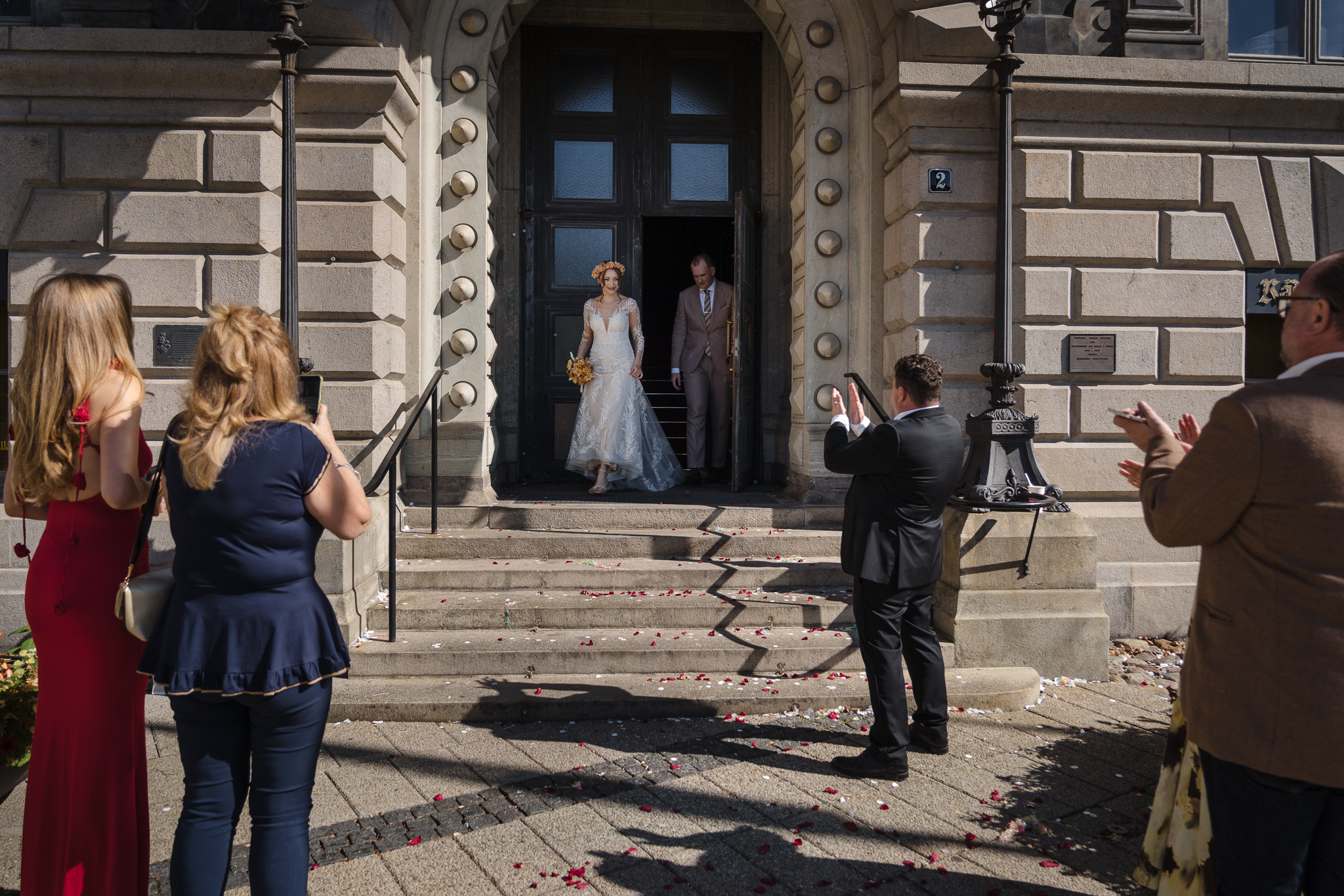 Ut ur Rådhuset Brudpar i porten till Malmö Rådhus med gäster och rosenblad på marken – bröllopsfotograf Malmö